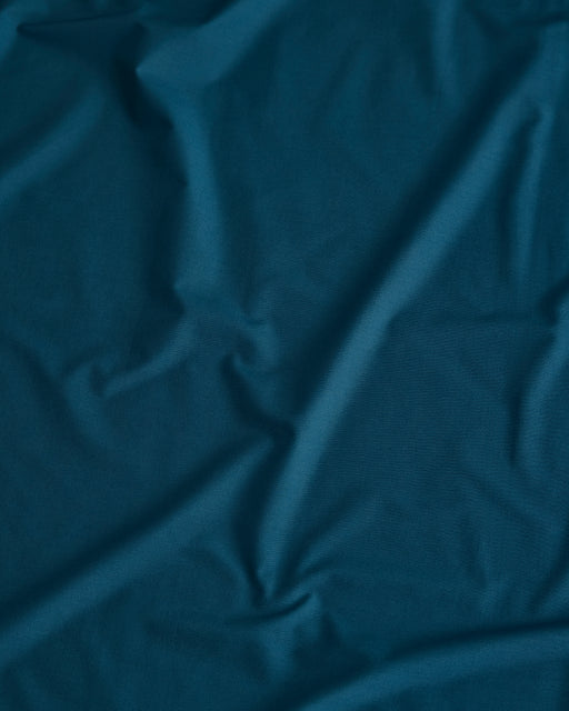 Close-up of the Bed Threads Aegean Organic Cotton in dark teal, showing visible folds and creases that create subtle shadows and texture on the percale surface.