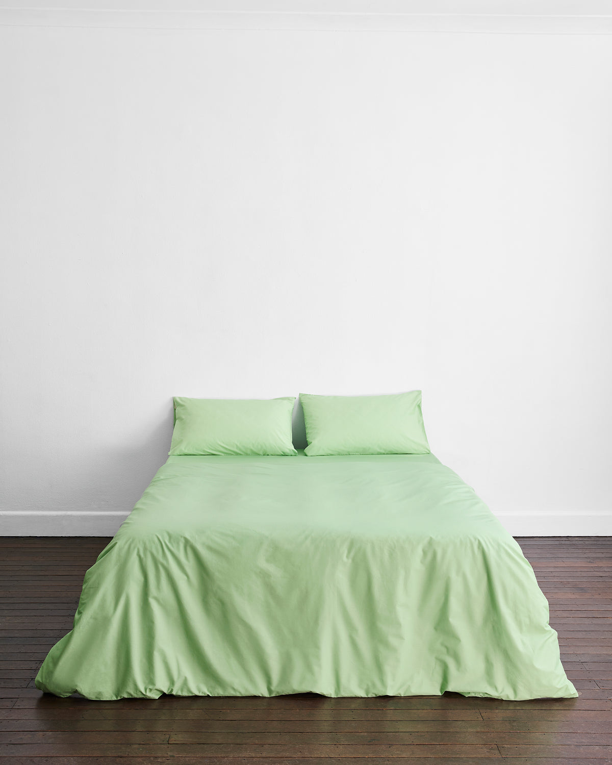A bed with the Bed Threads Apple Organic Cotton Duvet Cover and two matching pillows sits against a white wall on a dark wooden floor.