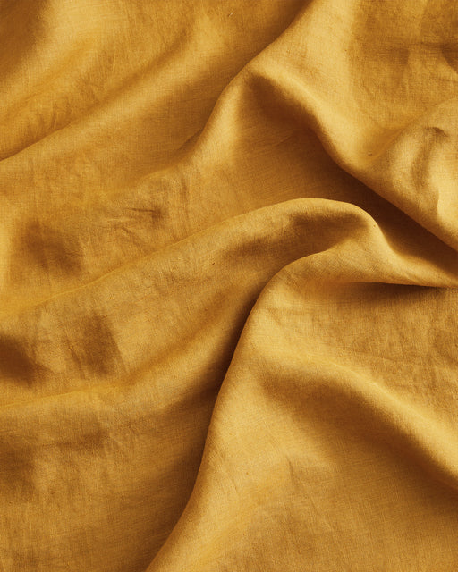 A close-up of the Turmeric 100% French Flax Linen Duvet Cover Set by Bed Threads showcases mustard yellow fabric with gentle creases and soft shadows—ideal for adding luxury and texture to your bedding.