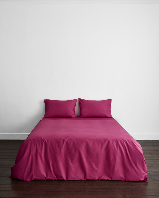 A bed with a Berry Organic Cotton Duvet Cover and two matching pillows by Bed Threads is neatly arranged against a white wall on a dark wooden floor.