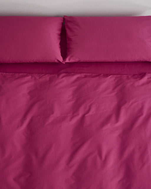 A neatly made bed features the Berry Organic Cotton Bedding Set by Bed Threads—bright magenta, GOTS certified, with pillowcases and a duvet cover, seen from above. Two pillows rest side by side at the head of this inviting set.