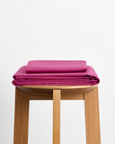 The Bed Threads Berry Organic Cotton Sheet Set, neatly folded, rests on a light wooden stool against a plain white background.
