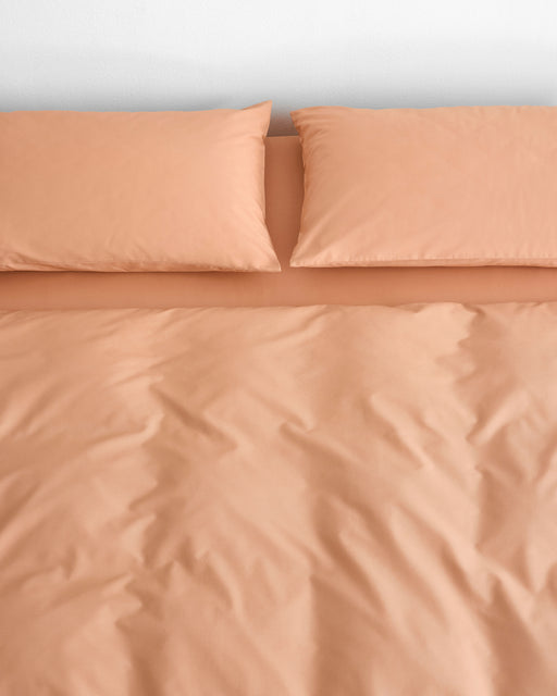 Butterscotch Organic Cotton Pillowcases (Set of Two) from Bed Threads, in a peach shade, styled on a neatly made bed with a duvet and viewed from above against a white wall background.