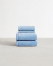 Set of two sky blue face washers and two hand towels in 100% cotton terry stacked on a light grey surface with a white background.  - view