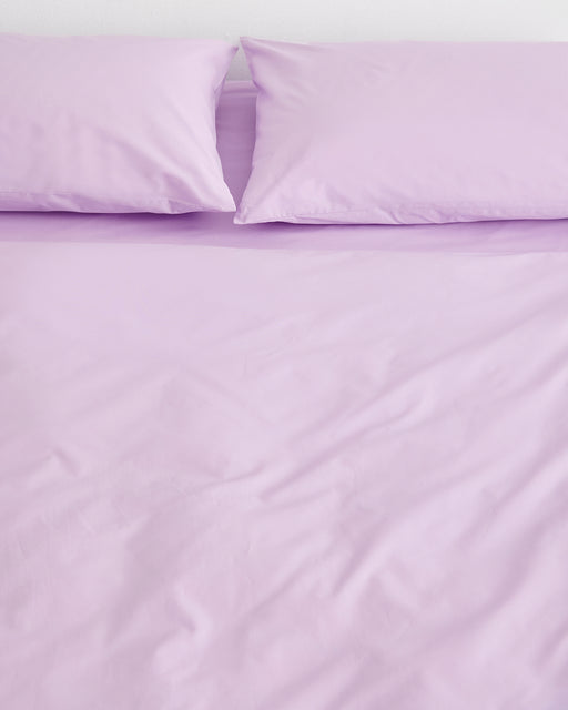 A neatly made bed with Violet 100% Organic Cotton Pillowcases (Set of Two) by Bed Threads, shown from above. The light purple pillowcases appear smooth and inviting, with gentle creases adding a relaxed touch.