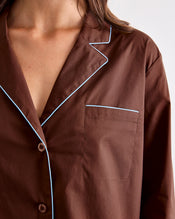 A close-up of a person wearing the Bed Threads Espresso & Sky Piped Long Sleeve Shirt, featuring white contrast piping along the collar, pocket, and edges. This cotton shirt has a smooth finish and includes a chest pocket. - view