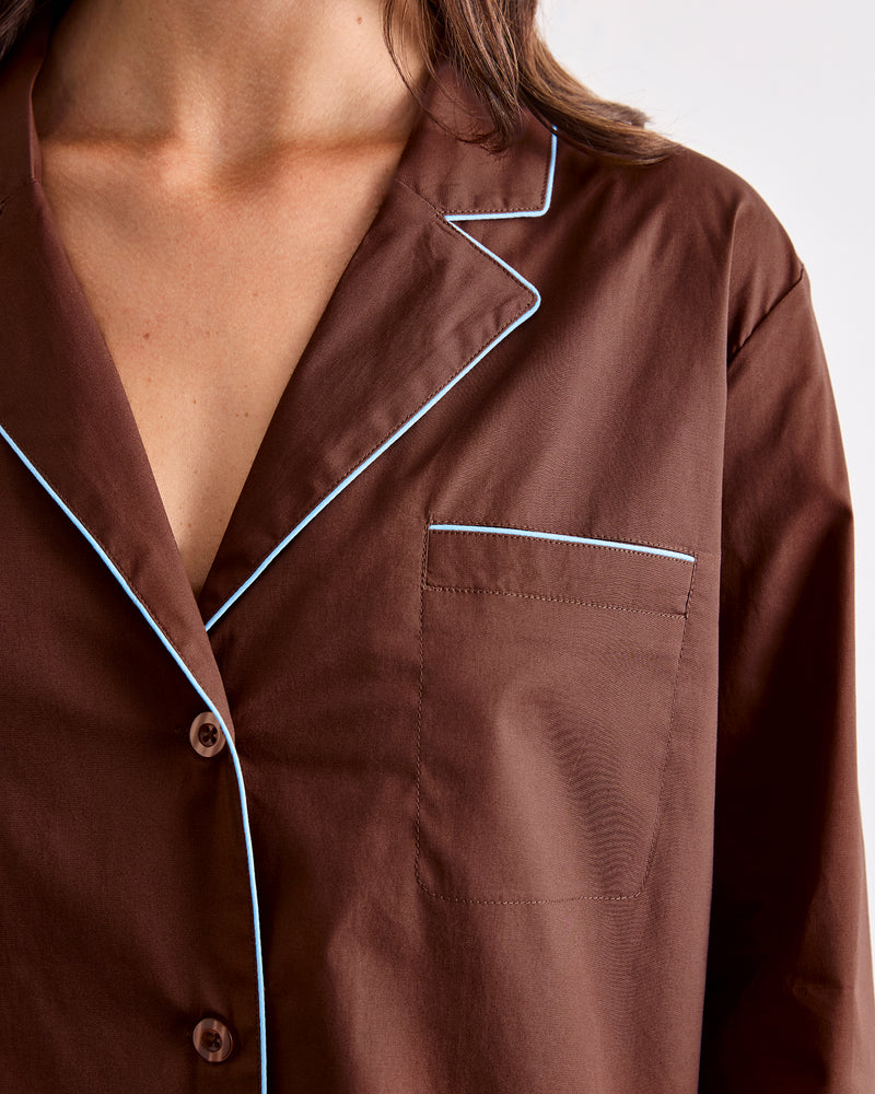 A close-up of a person wearing the Bed Threads Espresso & Sky Piped Long Sleeve Shirt, featuring white contrast piping along the collar, pocket, and edges. This cotton shirt has a smooth finish and includes a chest pocket.