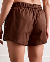 A close-up of a person wearing Bed Threads’ Espresso & Sky Piped Shorts, shown from the back. These breathable cotton sleep shorts feature an elastic waistband and are pictured indoors against a plain background. - view