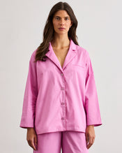 A woman stands barefoot on wooden floorboards, facing away from the camera, wearing the Bed Threads Bubblegum & Berry Piped Long Sleeve Shirt in a plain room with white walls. - view