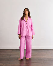 A person stands barefoot on a wooden floor, wearing loose high-waisted pink pants from the Bed Threads Bubblegum & Berry Piped Long Sleep Set; the elastic waistband is visible, but the upper body is not shown. - view