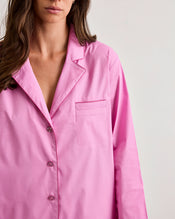 A woman wears the Bed Threads Bubblegum & Berry Piped Long Sleeve Shirt, a loose-fitting, bright pink cotton pyjama-style button-up with a chest pocket, standing against a plain light background. Her face is partially out of frame. - view