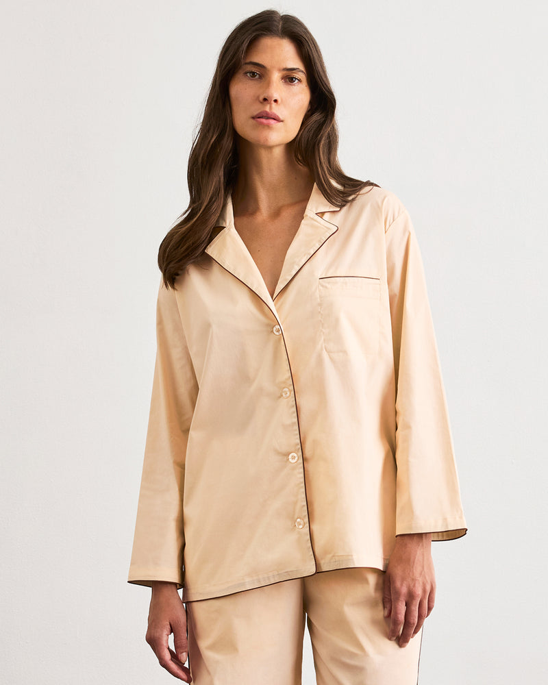 A person with long hair stands barefoot on a wooden floor, facing a plain white wall, wearing the Bed Threads Vanilla & Espresso Piped Long Sleeve Shirt.