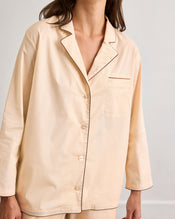 A person wears the Bed Threads Vanilla & Espresso Piped Long Sleeve Shirt, a light beige cotton set with contrast piping, chest pocket, and long sleeves. The image is cropped at the neck and knees. - view
