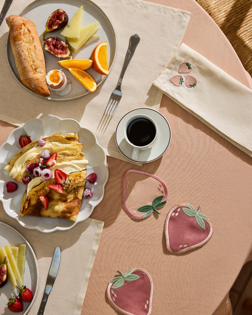 A breakfast table with an omelet, fruit, cheese, figs, orange slices, baguette, coffee, and embroidered strawberry linens is set on the Terracotta 100% French Flax Linen Tablecloth by Bed Threads for a luxurious touch.