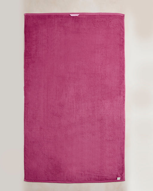 The Berry Cotton Terry Bath Sheet by Bed Threads is a large, rectangular magenta towel displayed on a light surface, highlighting its soft texture and simple design—ideal for adding plush luxury to your bathroom.