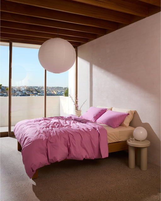 A bed with pink sheets, Bed Threads Bubblegum Organic Cotton King Pillowcases (Set of Two), and a white lamp.