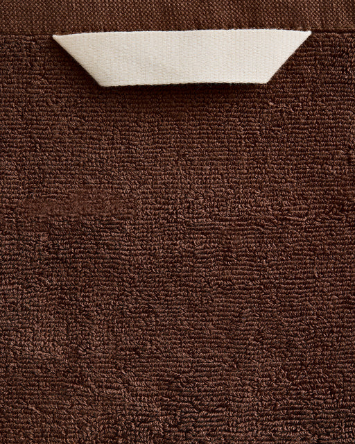 The Bed Threads Espresso Cotton Terry Bath Towels (Set of Two) feature highly absorbent, plush brown textured fabric with a small corner folded to reveal the white reverse side.