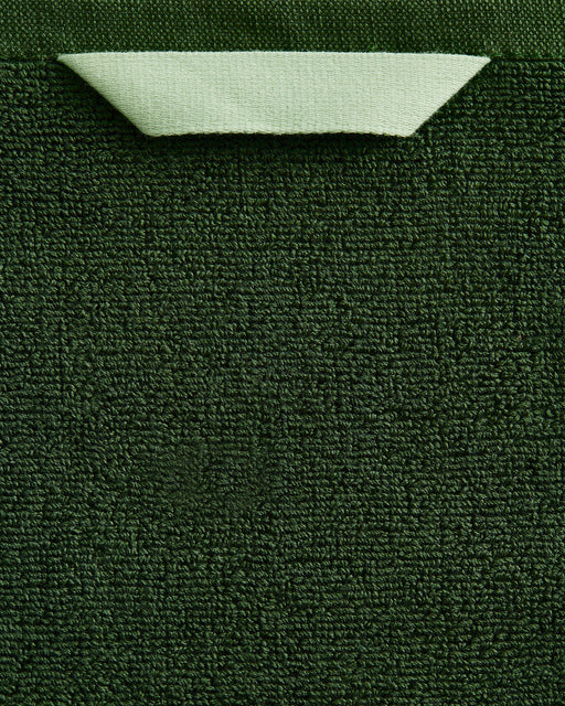 A close-up of the Bed Threads Moss Cotton Terry Bath Sheet Bundle shows its dark green textured cotton, with a light green fabric loop near the top edge, highlighting its highly absorbent material.