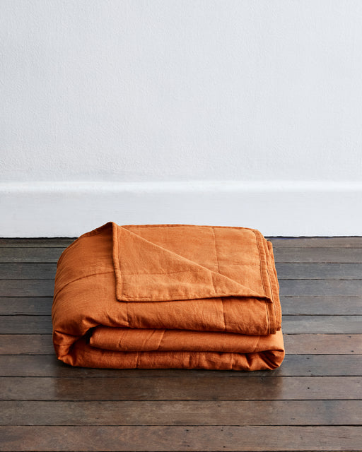 Folded orange blanket on a wooden surface with a white wall background