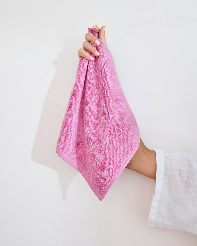 A modern white bathroom sink with a bar of soap, a brush, and two Bubblegum 100% Cotton Terry Face Washers by Bed Threads folded on the countertop. A matching pink bathmat completes the minimal, tidy scene designed to be gentle on skin.