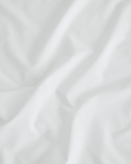 The Crisp White Organic Cotton by Bed Threads features soft folds and subtle shadows on a smooth, slightly textured GOTS certified surface, giving it a light, airy look with natural creases throughout.