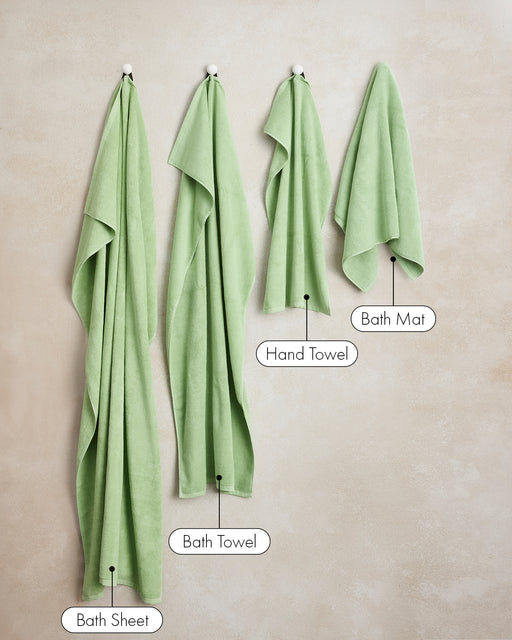 A set of two light green Apple Cotton Terry Hand Towels by Bed Threads, made from 100% cotton, hang on hooks against a beige wall. Each towel is highly absorbent and soft.