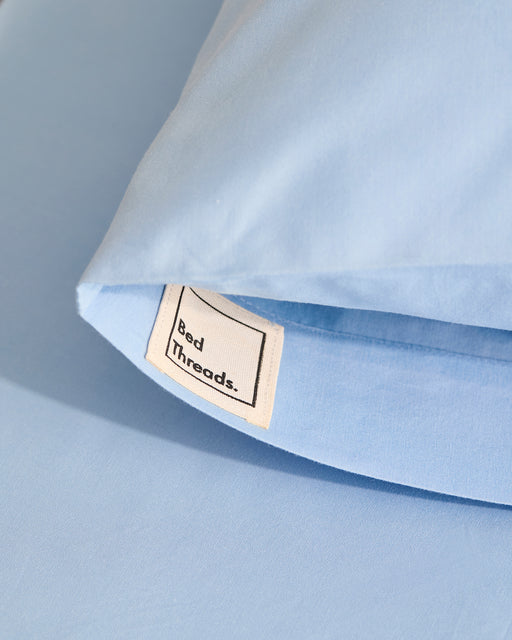 A close-up of Sky Organic Cotton Pillowcases (Set of Two) in light blue by Bed Threads, with a fabric label partially visible at the pillow’s opening.