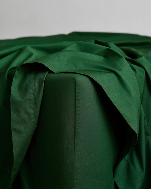 A close-up of a bed corner featuring Bed Threads’ Apple & Moss Organic Cotton Bedding Bundle with GOTS certified, smooth percale duvet cover draped elegantly over the edge against a plain, light background.