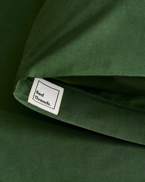 A close-up of Bed Threads' Moss Organic Cotton Pillowcases (Set of Two) in dark green, showing a white fabric label, highlights their breathable design for a comfortable night's sleep.