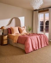 A bed styled with Bed Threads Terracotta & Pink Clay 100% French Flax Linen Swirl European Pillowcases, a beige upholstered headboard, and a side table topped with a glass vase of green foliage. - view