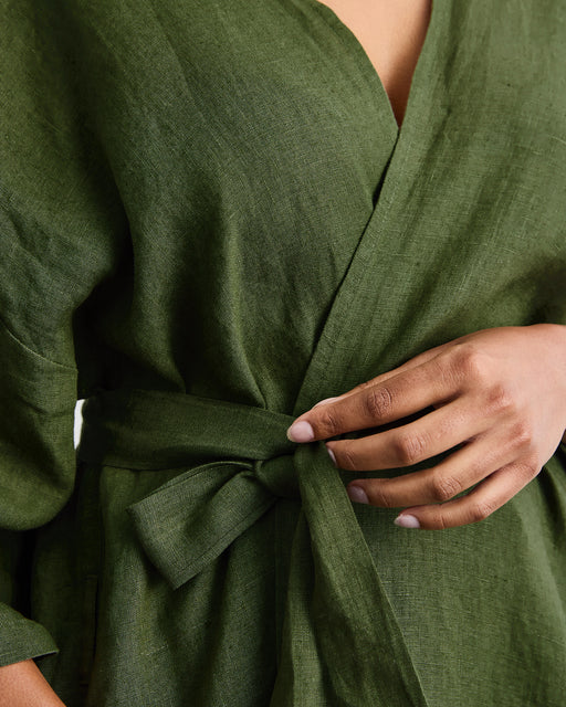 A person ties the waist belt of the Cabana Short Robe in Olive by Bed Threads, shown from shoulders to hips, with one hand adjusting the bow and the other resting at their side.