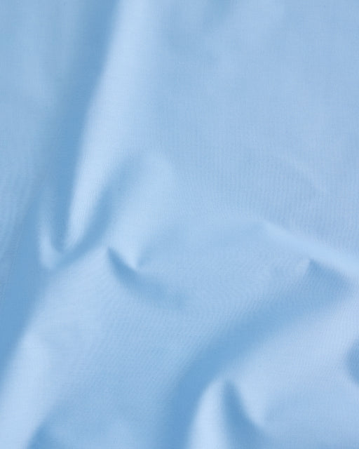The Sky Organic Cotton Flat Sheet by Bed Threads features light blue organic cotton percale with subtle creases, soft shadows, and a smooth texture—perfect for gentle comfort against your skin.