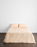 A neatly made bed features the Bed Threads Vanilla Organic Cotton Bedding Set with two matching pillows, centered against a plain white wall on a dark wooden floor for a minimal and simple look.
