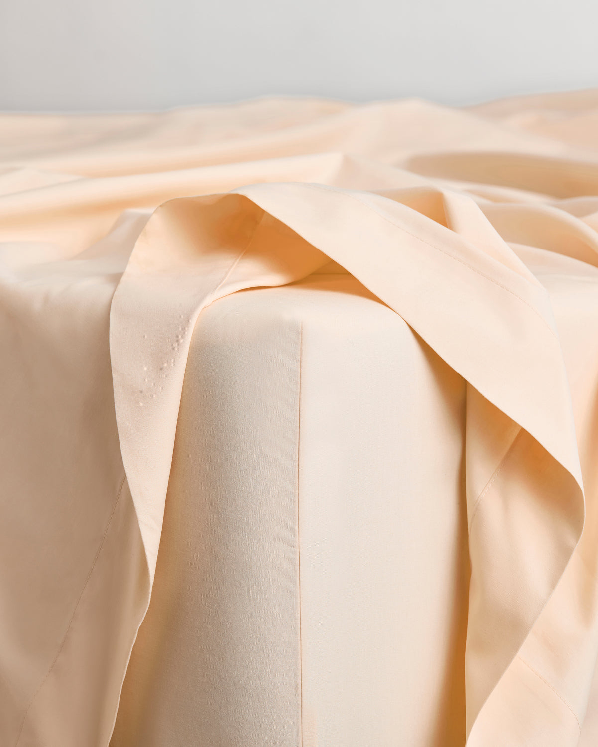 A close-up of a neatly made bed showcases the Bed Threads Espresso & Vanilla Organic Cotton Bedding Bundle. The fitted sheet hugs the mattress, while the flat sheet and organic cotton layers drape casually over one corner.