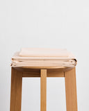 The Bed Threads Vanilla Organic Cotton Sheet Set is neatly folded and displayed on a wooden stool against a plain white background.