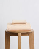 A neatly folded Bed Threads Vanilla Organic Cotton Duvet Cover Set, including bed sheets and pillowcases, rests on a wooden stool against a plain white background.