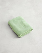 A neatly folded Apple 100% Cotton Terry Bath Mat by Bed Threads in light green rests on a plain, light-colored surface. - view