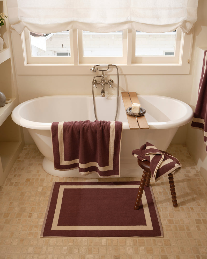 Close up of a freestanding bath tub with cotton terry towels in a cacao colour with creme border.