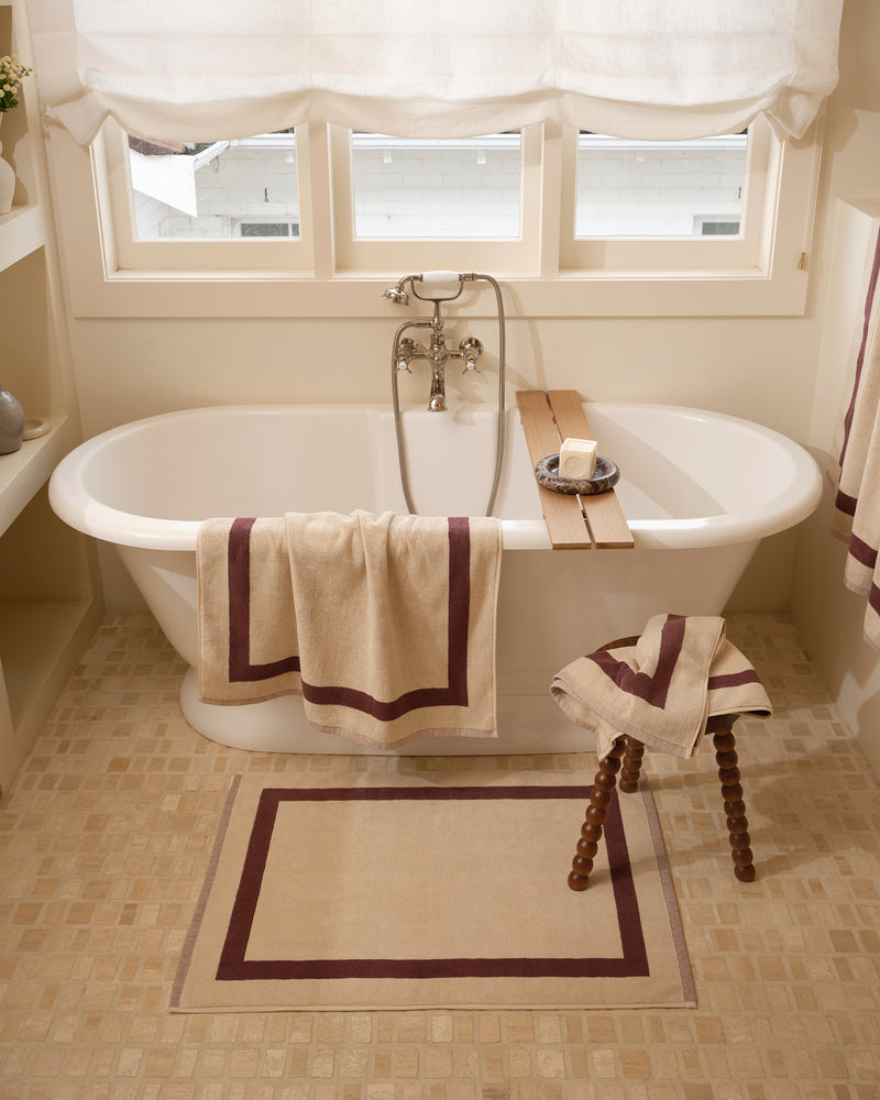 Close up of a freestanding bath tub with cotton terry towels in a creme colour with cacao border.