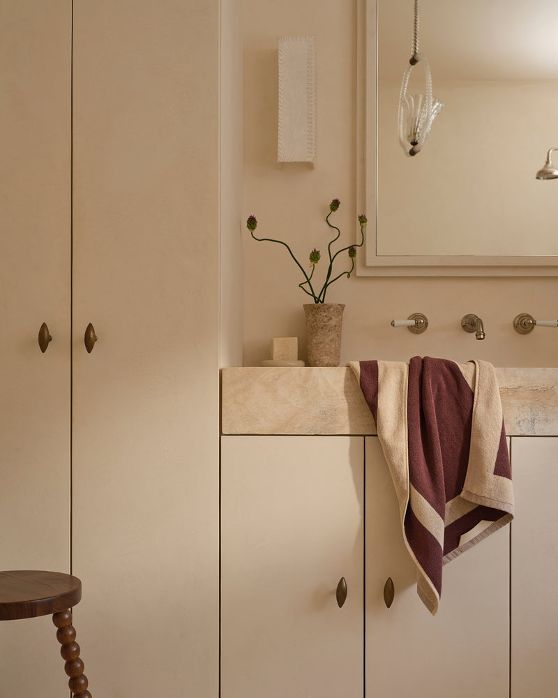 Neutral bathroom with cotton terry hand towel in creme and cacao hanging near sink.