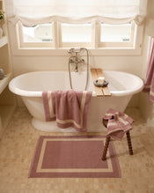 Close up of a freestanding bath tub with cotton terry towels in a lavender colour with creme border. - view