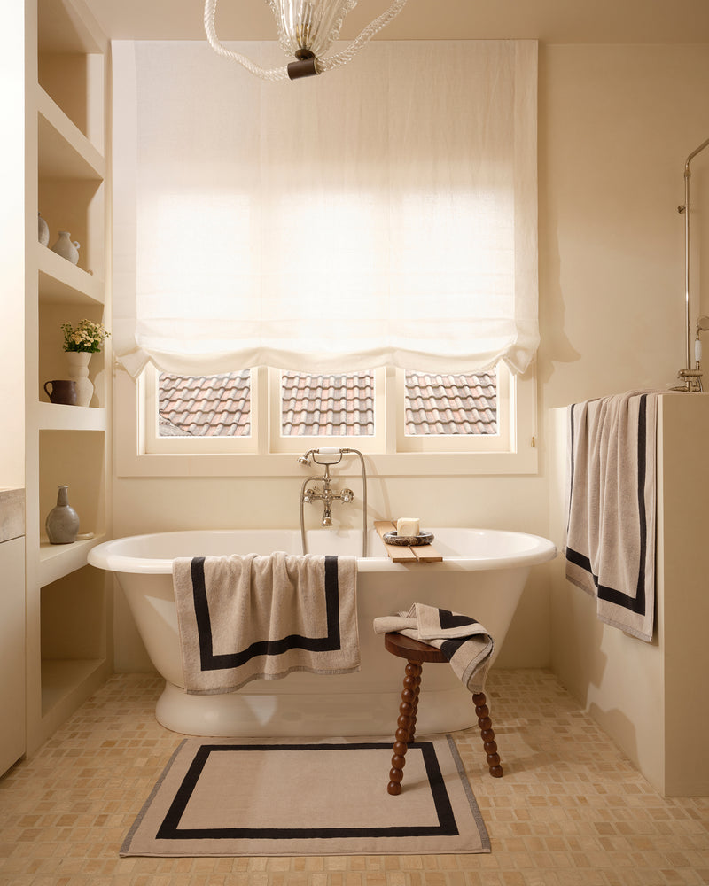 Neutral bathroom with freestanding bath tub and cotton terry towels in an oatmeal colour with charcoal border.