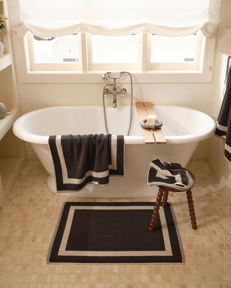 Close up of a freestanding bath tub with cotton terry towels in a charcoal colour with oatmeal border.