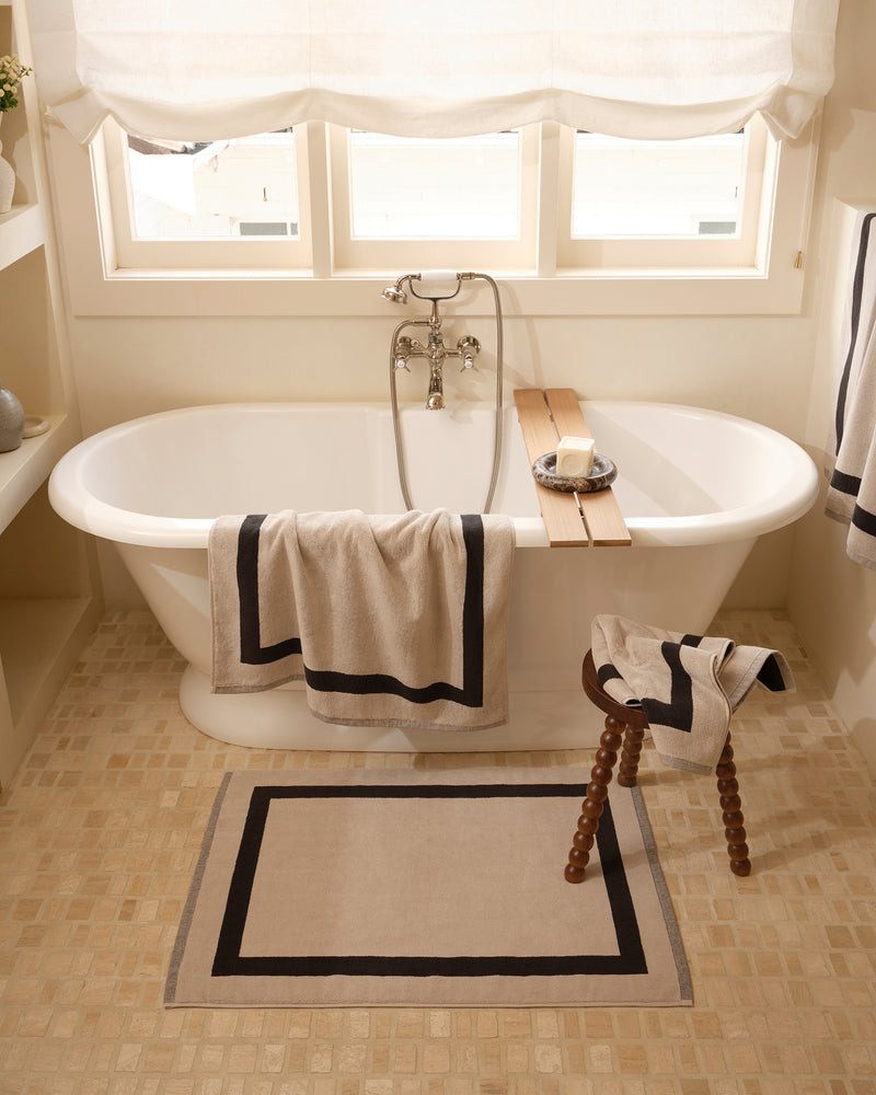 Close up of a freestanding bath tub with cotton terry towels in an oatmeal colour with charcoal border.