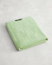 The Bed Threads Apple 100% Cotton Terry Bath Sheet, neatly folded in light green, rests on a light gray textured surface, bringing a touch of luxury to your space. - view