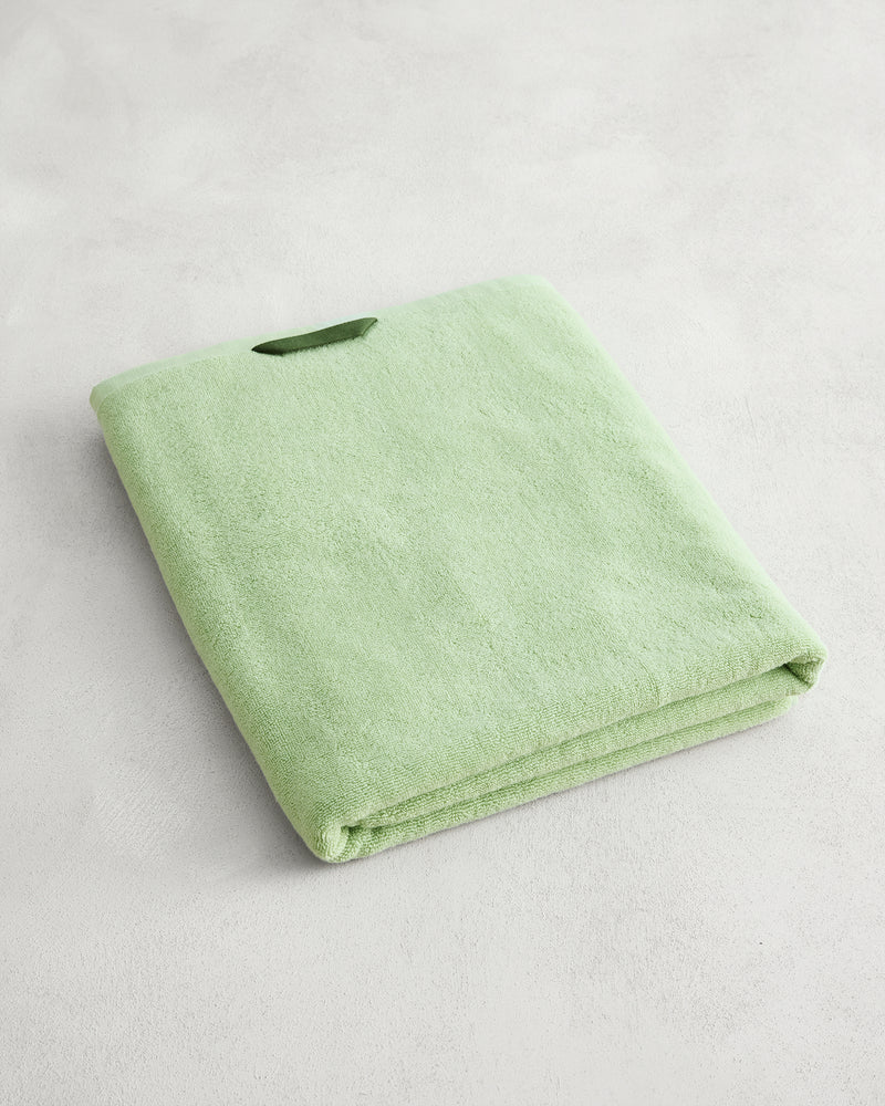 The Bed Threads Apple 100% Cotton Terry Bath Sheet, neatly folded in light green, rests on a light gray textured surface, bringing a touch of luxury to your space.