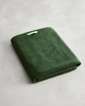 The Moss 100% Cotton Terry Bath Sheet by Bed Threads, in deep green with a white tag, rests on a light gray surface—ideal for anyone seeking plush, quick-drying towels. - view