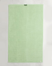 A set of two Apple 100% Cotton Terry Bath Sheets by Bed Threads, in light green, each rectangular with a dark green loop near the top edge and a white tag at the bottom right, laid flat on a white surface. - view