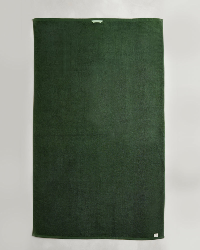 A set of two large, rectangular Moss 100% Cotton Terry Bath Sheets by Bed Threads is displayed flat on a light background. Each dark green towel features a small white tag near the edge and a convenient fabric loop at the top center.