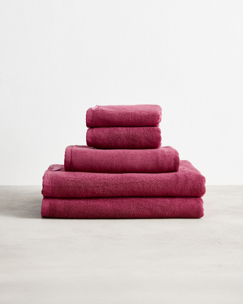 Five Berry 100% Cotton Terry Bath Sheets by Bed Threads are neatly stacked in a pyramid shape on a light surface against a plain white background.